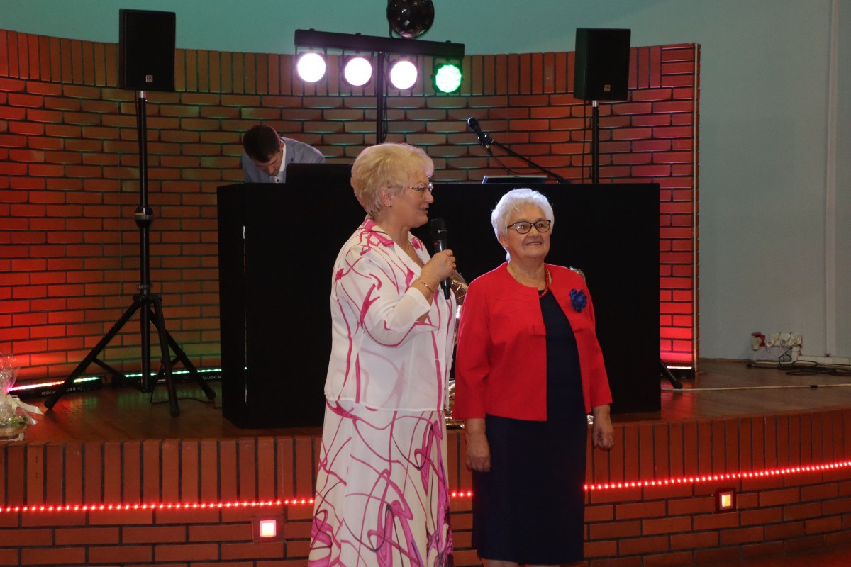 Dwie kobiety stoją przed sceną, jedna trzyma mikrofon