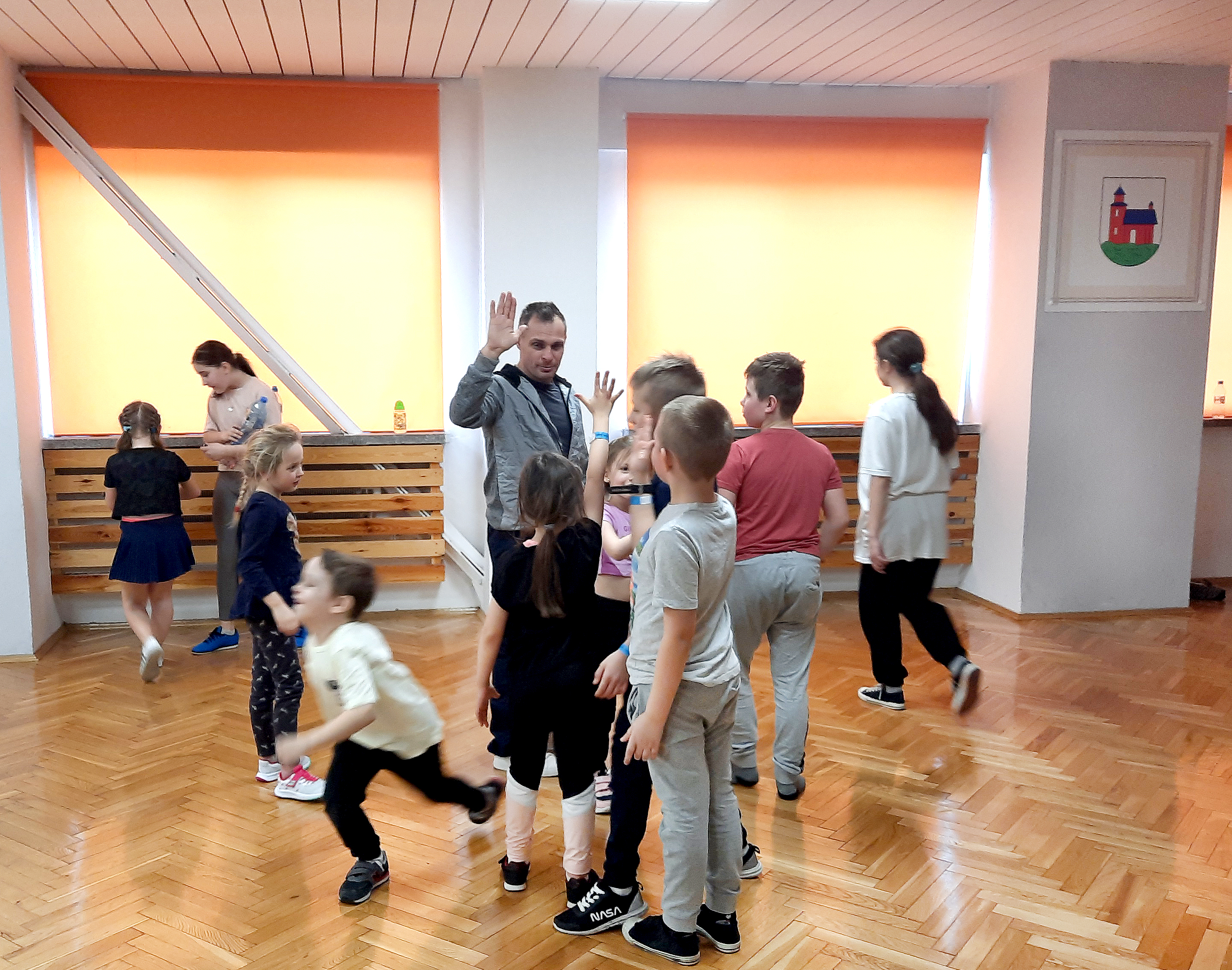 Dzieci po skończonych zajęciach z breakdance przybijają "piątkę" z instruktorem