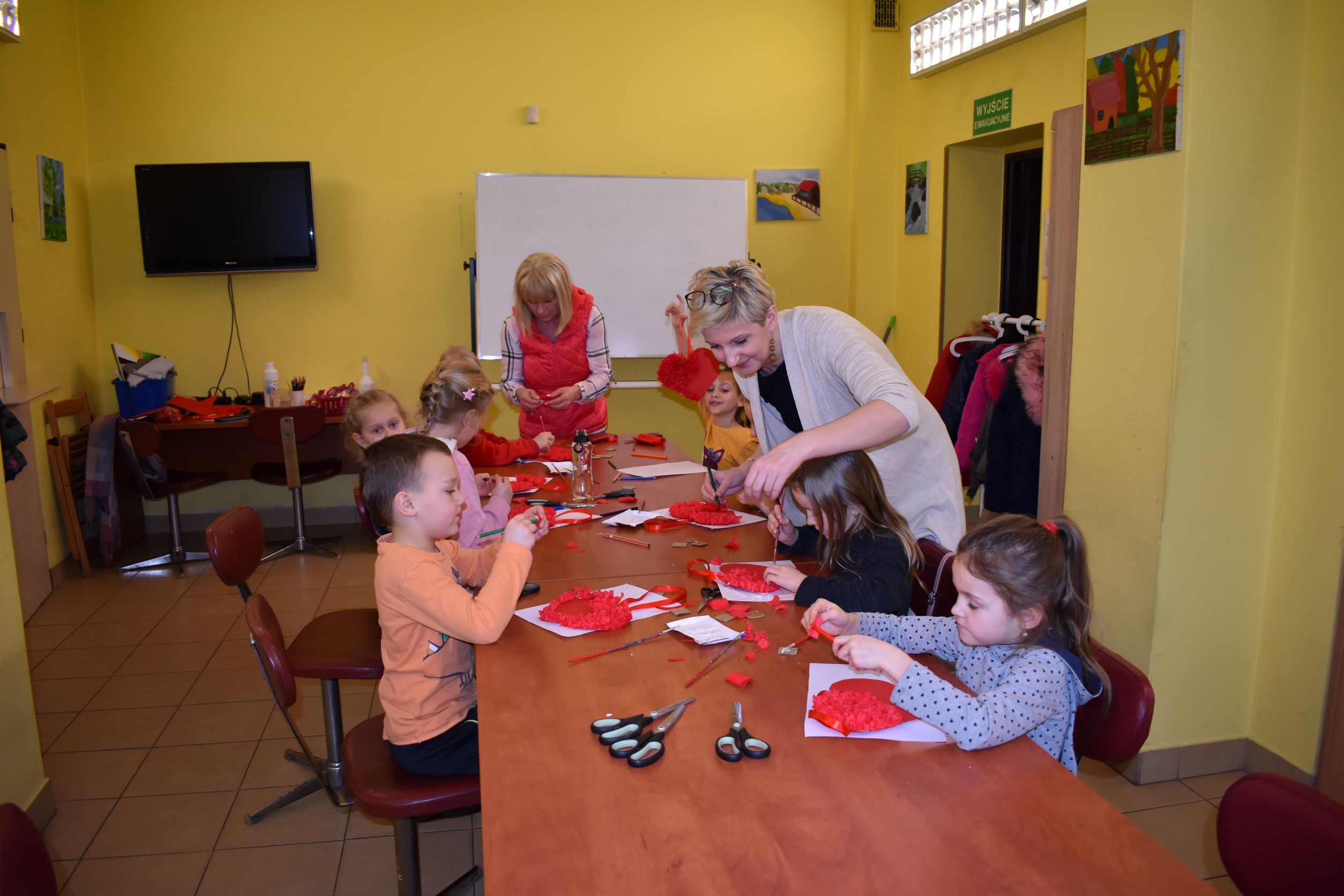 Dzieci siedzące przy stole tworzące czerwone serca z papieru