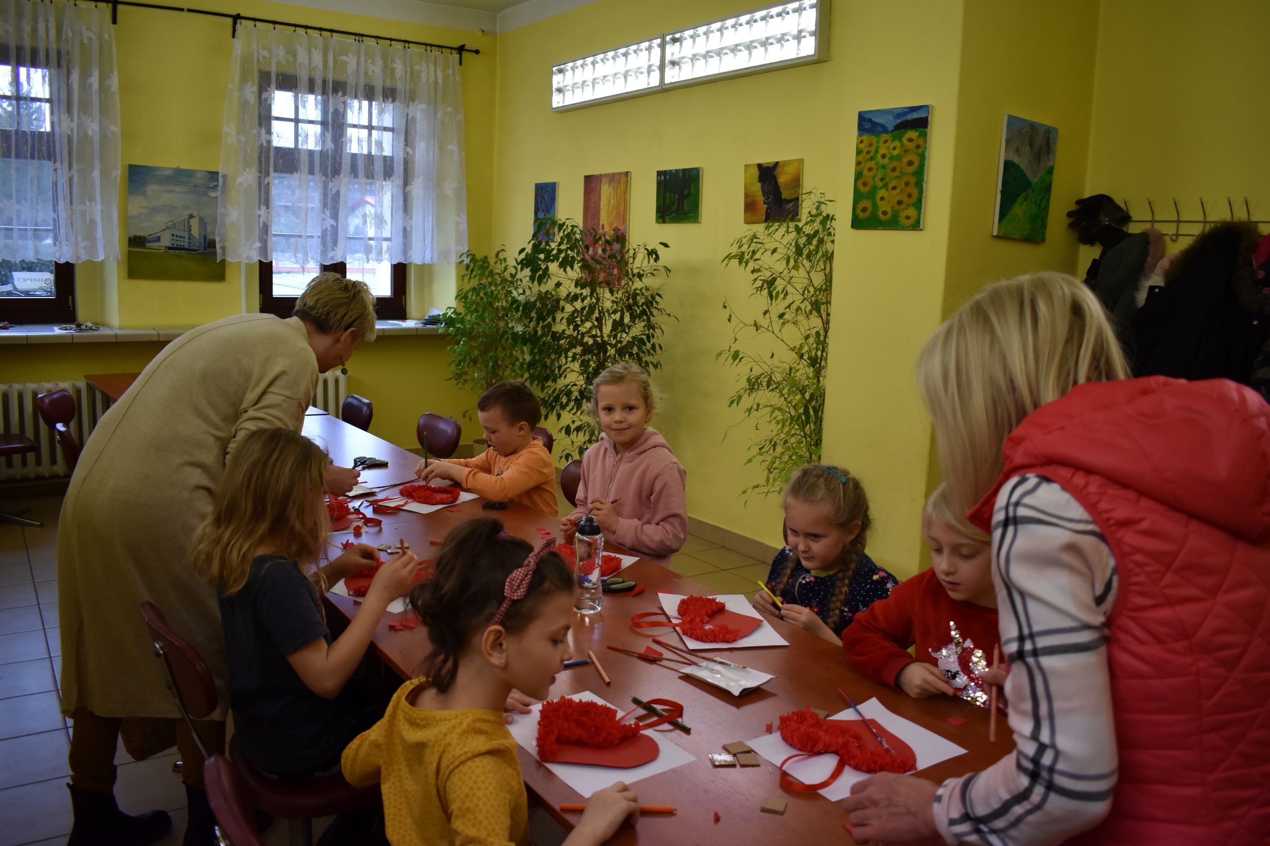 Dzieci podczas pracy z instruktorami w MOK. Siedzą przystole i tworzą czerwone serca