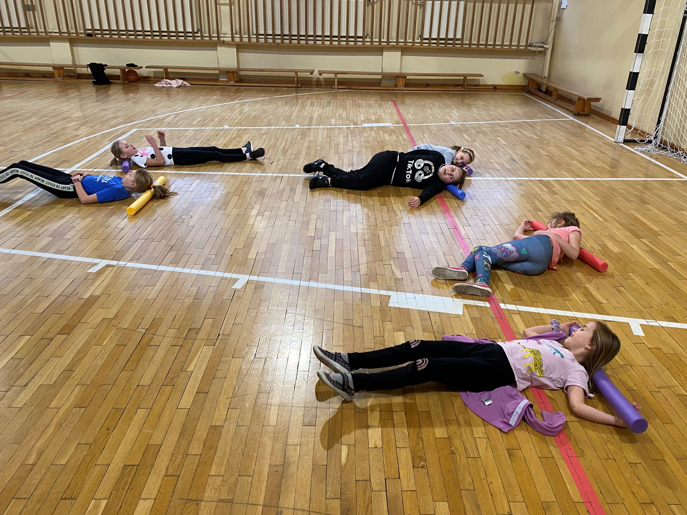 Dzieci leżą na ziemi podczas zabawy z "makaronami" na sali gimnastycznej