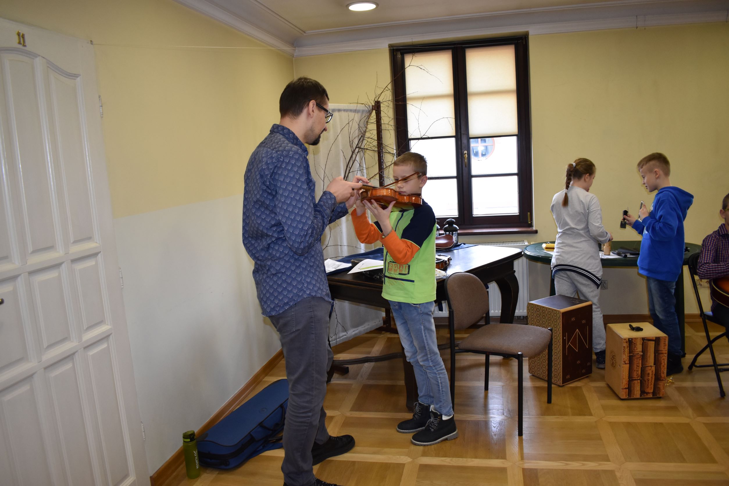 Dzieci podczas zajęć z instruktorem, na pierwszym planie chłopiec z instruktorem podczas nauki gry na skrzypcach