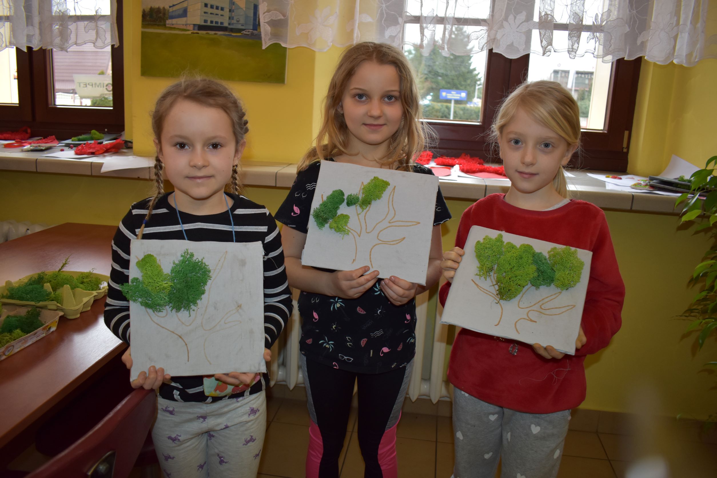 Trzy dziewczynki prezentują swoje prace stworzone podczas zajęć w Miejskim Ośrodku Kultury 